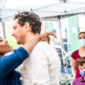 in the foreground a pair of actors rehearses the preparation for a kiss, observed by stage manager and intimacy choreographer in the background.